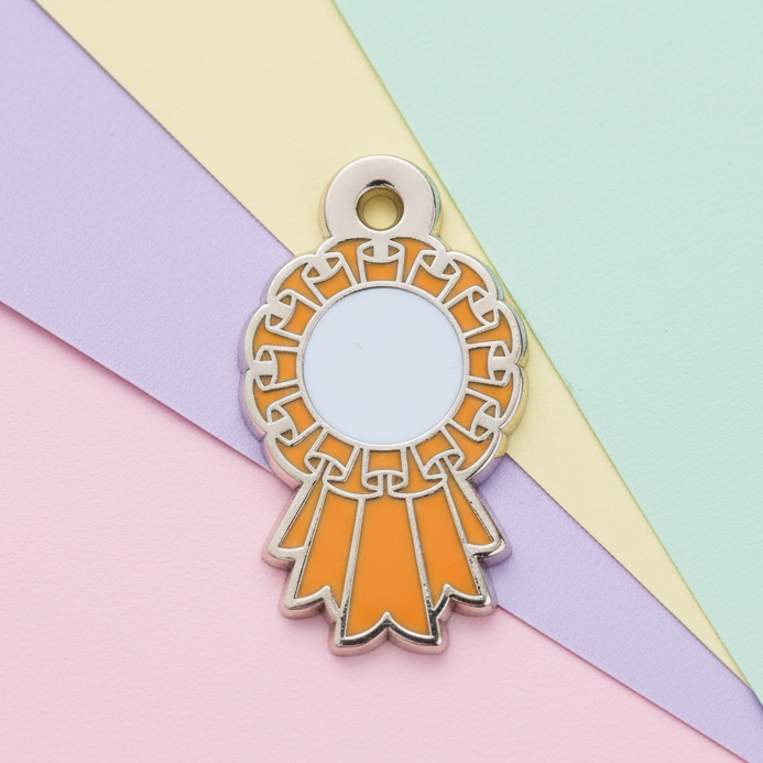 Enamel pin with orange ribbon design on a pink and white background